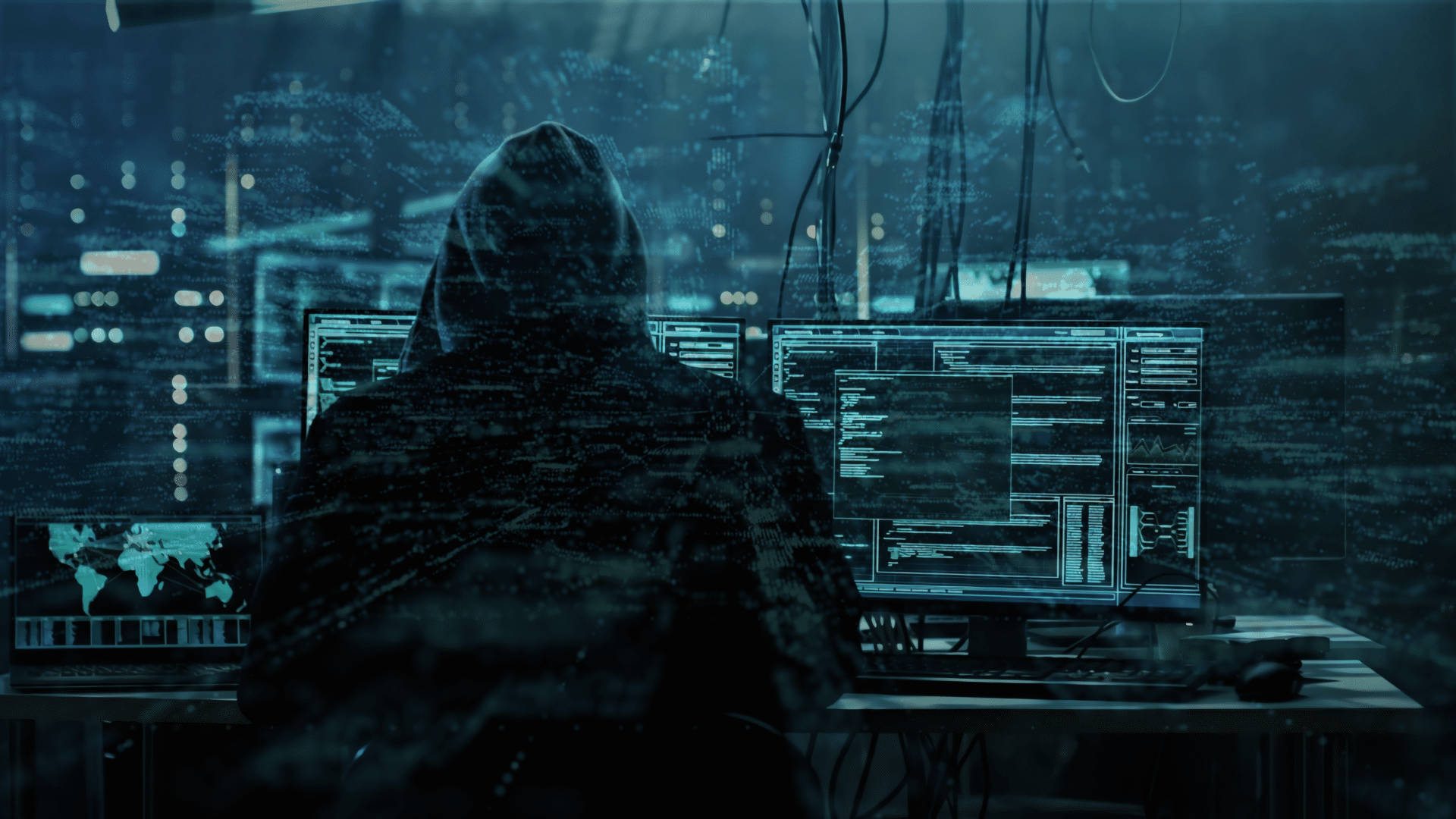image of a hacker in a hoodie sitting infront of multiple computers